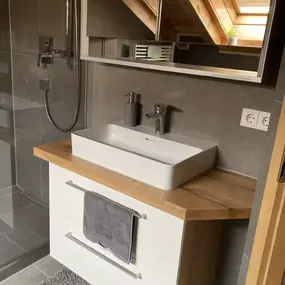 Modernes Badezimmer mit Waschtisch, Holzplatte, Spiegel und Dachfenster im Dachgeschoss.