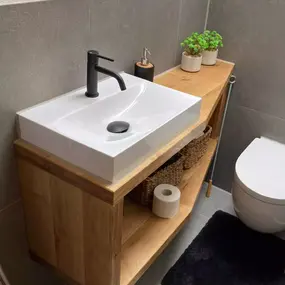 Modernes Badezimmer mit Holzwaschtisch, weißen Fliesen, Pflanzen und WC, minimalistisch gestaltet.