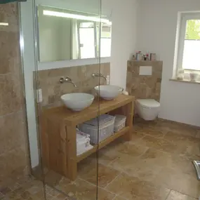 Modernes Badezimmer mit Natursteinfliesen, Holzwaschtisch, Doppelwaschbecken und Glasdusche.