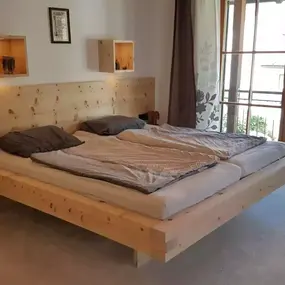 Modernes Schlafzimmer mit großem Massivholzbett, hellen Möbeln und Balkonzugang.